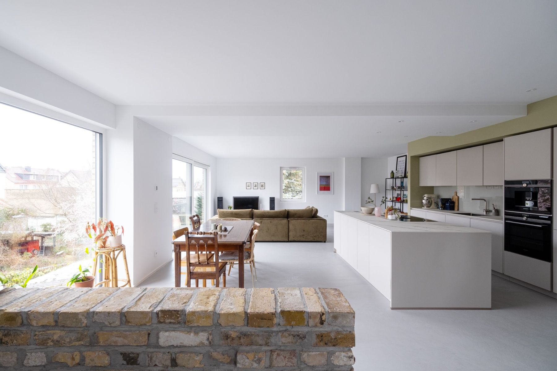 Appartement R, Wohnküche mit Ziegelmauer, Esstisch und großen Fenstern