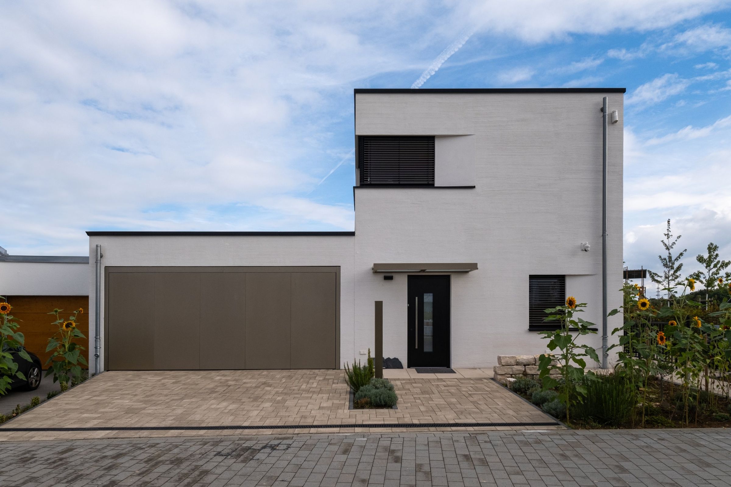 Haus H in Hochheim: Straßenansicht mit Garage, weißem Putzbau und Sonnenblumen
