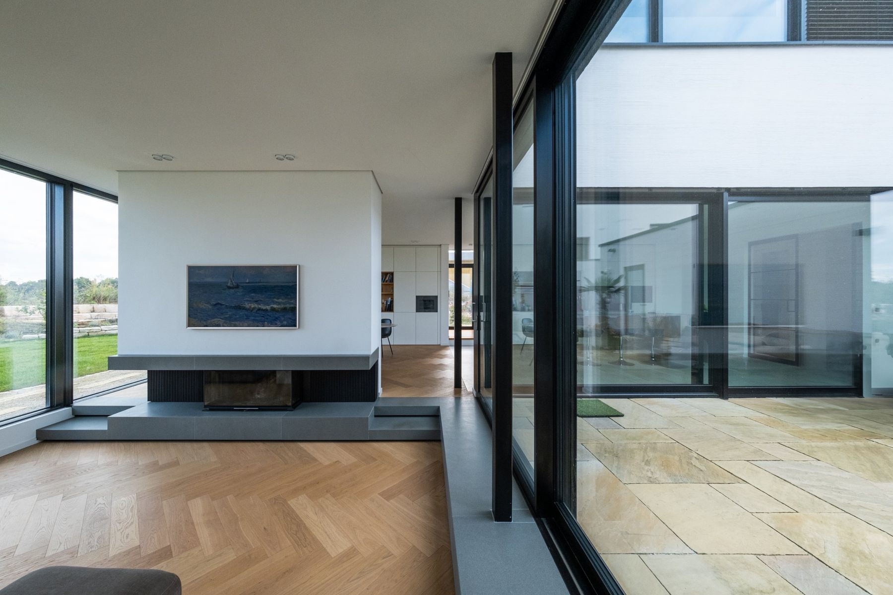 Haus H, Wohnraum mit freistehendem Kamin, Fischgrätparkett und Glasfront zum Hof