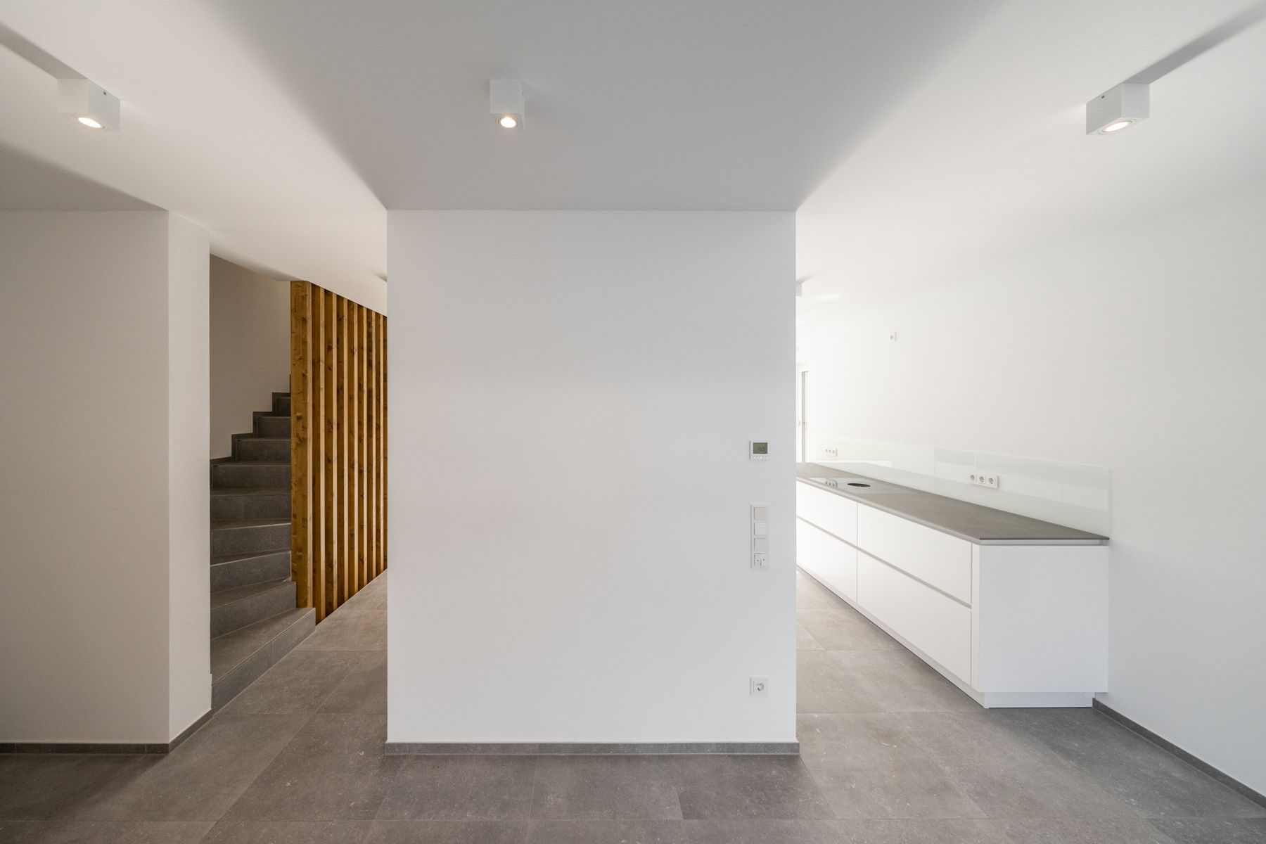 Haus M, Flur mit Holzlamellen am Treppenaufgang und weißer Küchenzeile