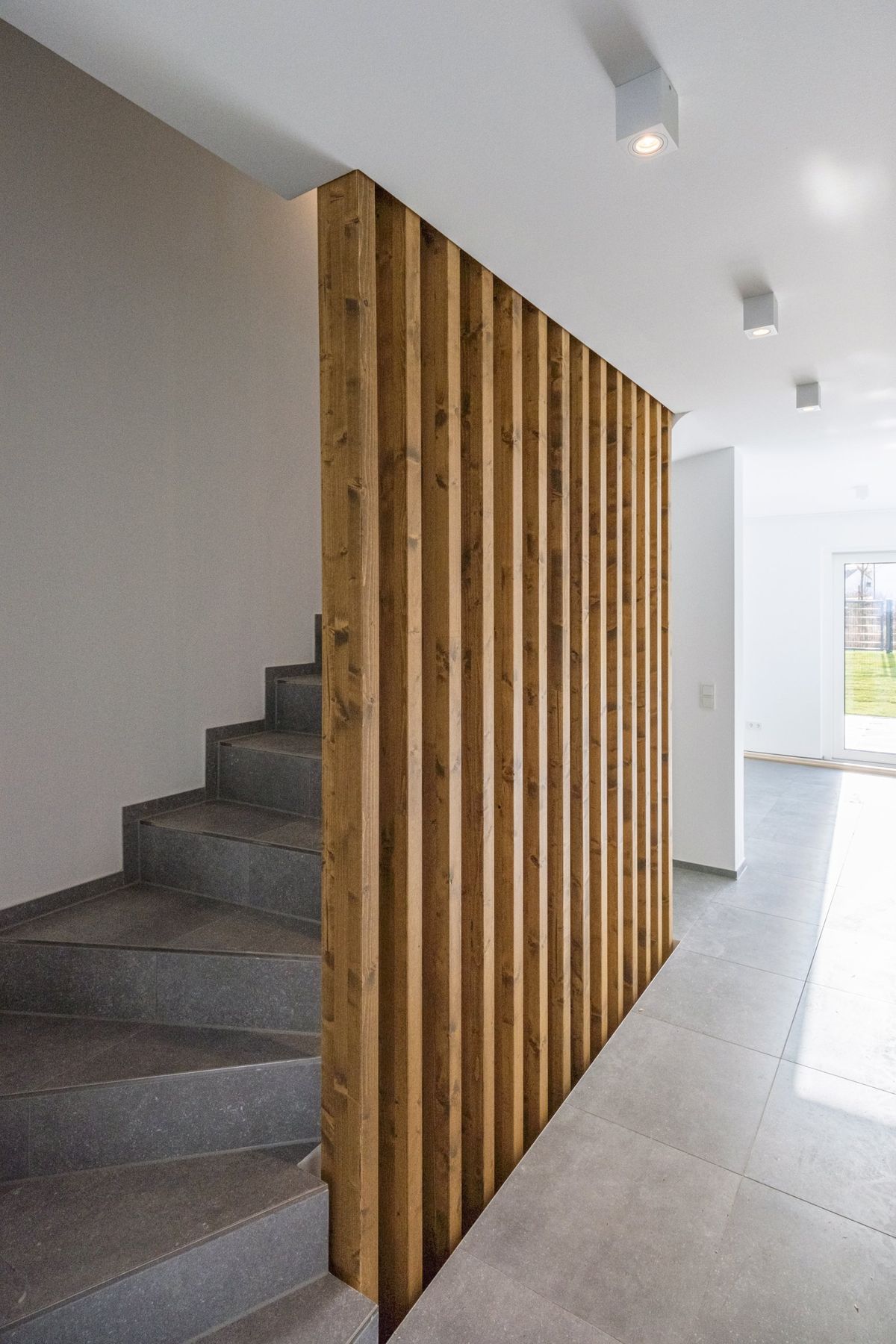 Haus M, Treppe aus Beton hinter einer Wand aus senkrechten Holzlamellen