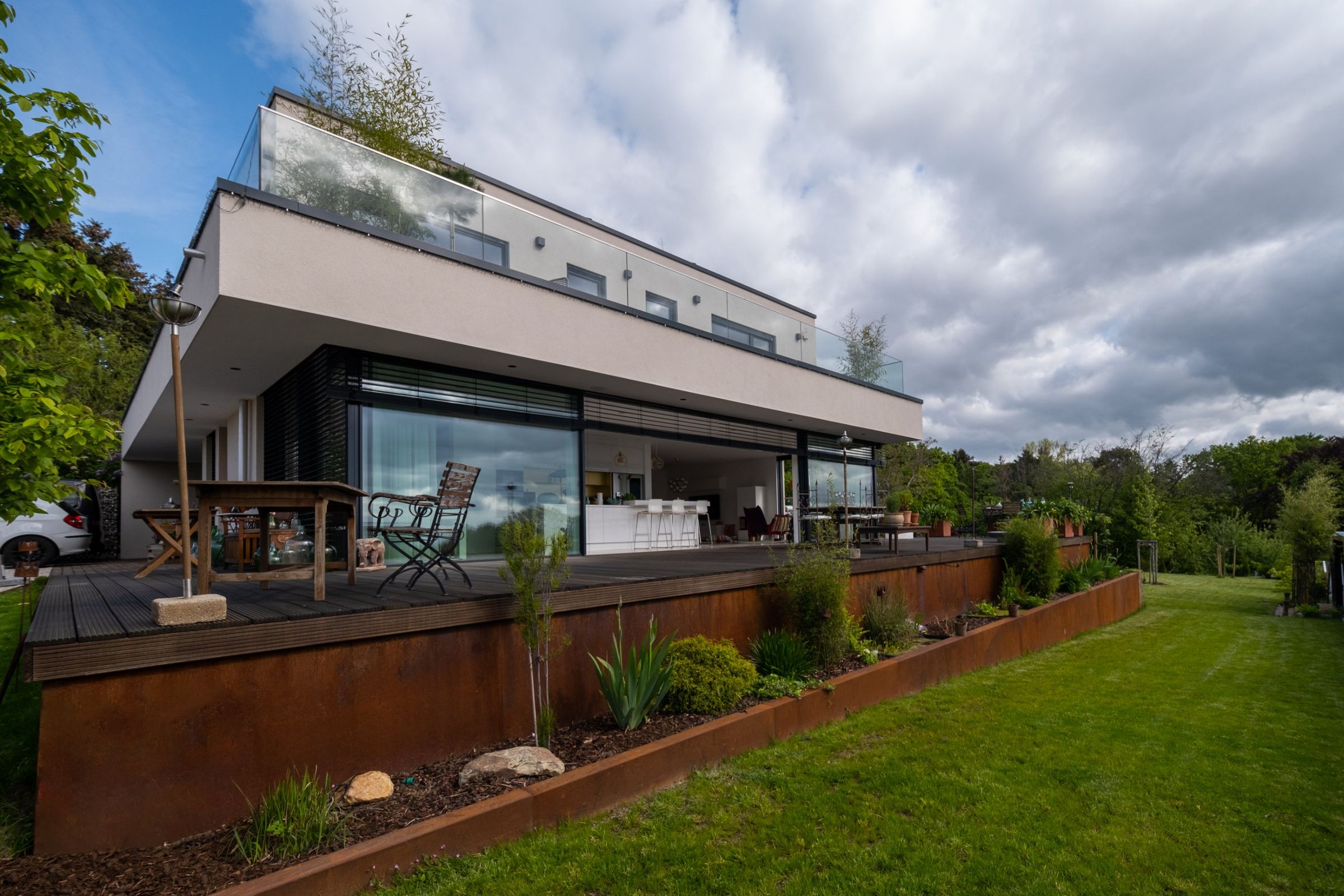 Haus RE in Wiesbaden: Gartenseite mit Cortenstahl-Stützwand, Terrasse und Glasfront