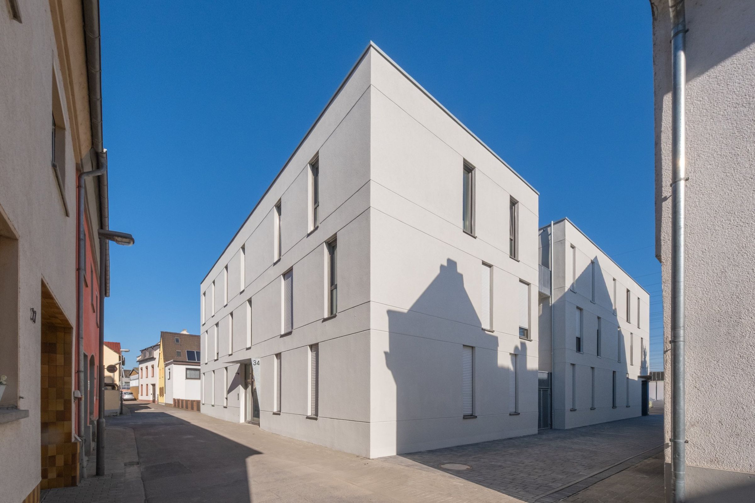 Mehrfamilienhaus K, Ansicht über Eck vor blauem Himmel in einer schmalen Gasse