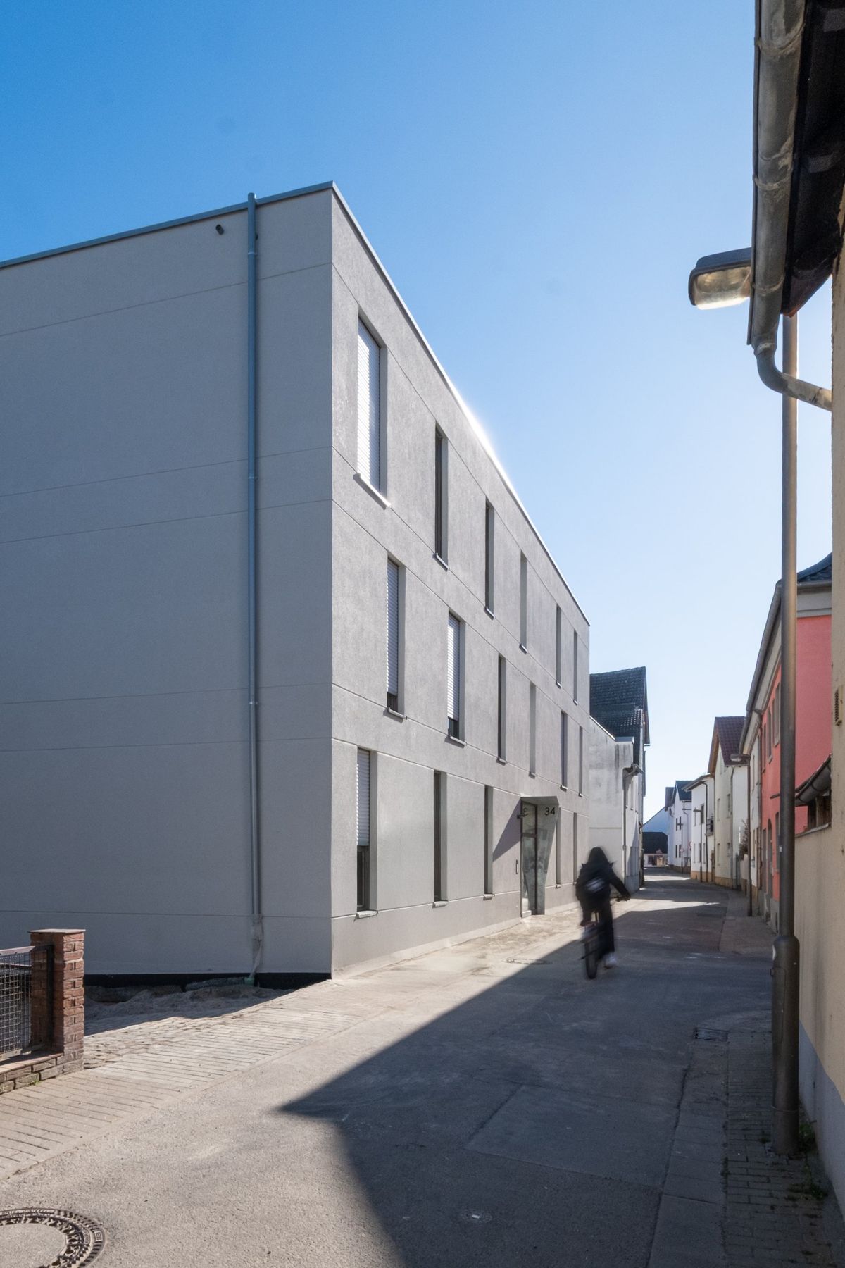 Mehrfamilienhaus K, Fassade entlang der Gasse mit Radfahrer im Schatten