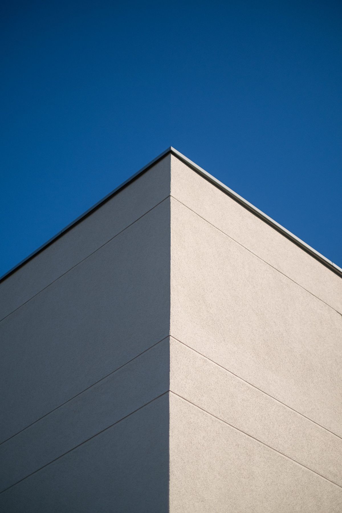 Mehrfamilienhaus K, Gebäudeecke mit heller Putzfassade vor tiefblauem Himmel