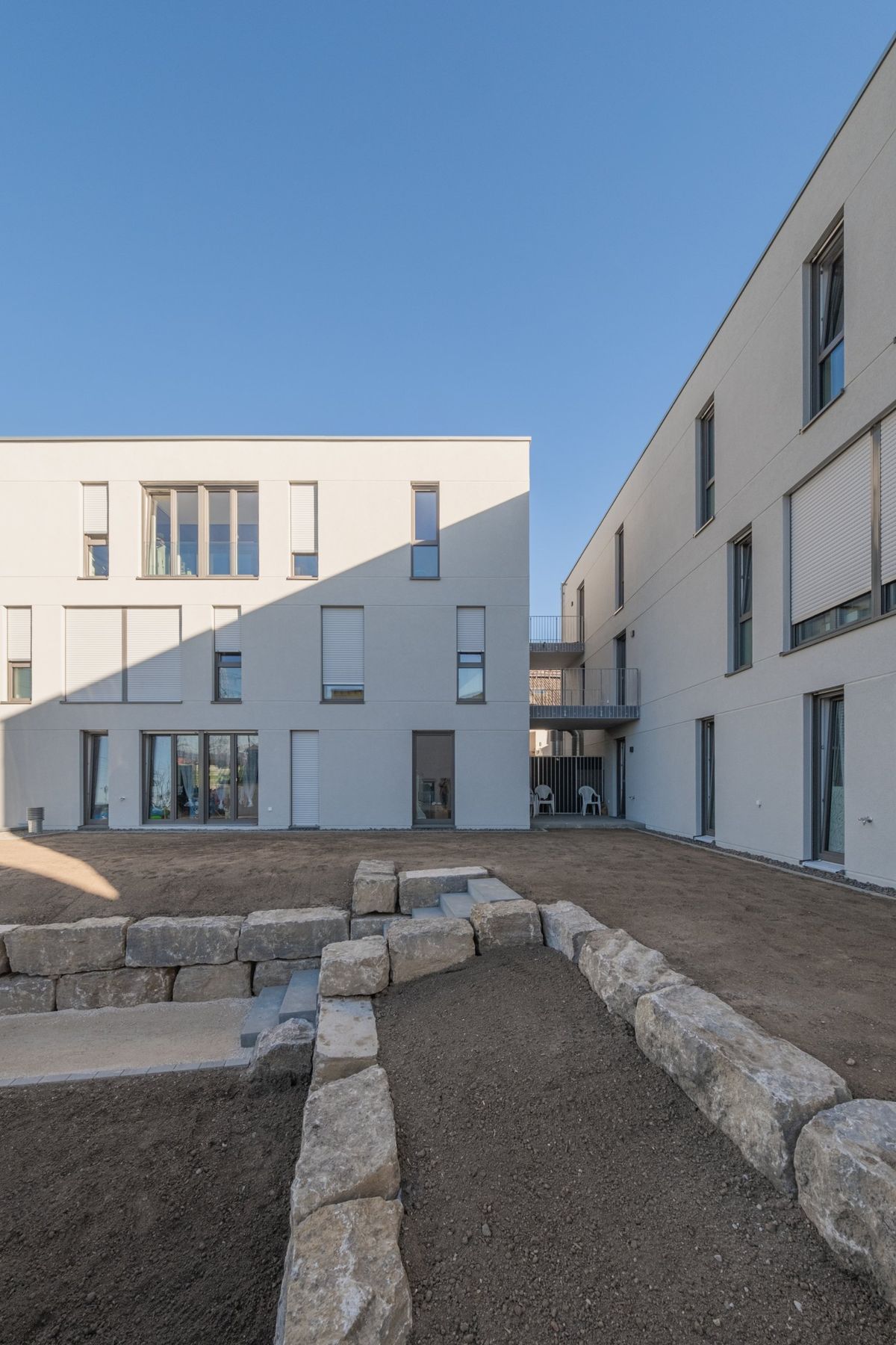 Mehrfamilienhaus K, Innenhof mit Natursteinblöcken zwischen zwei Baukörpern