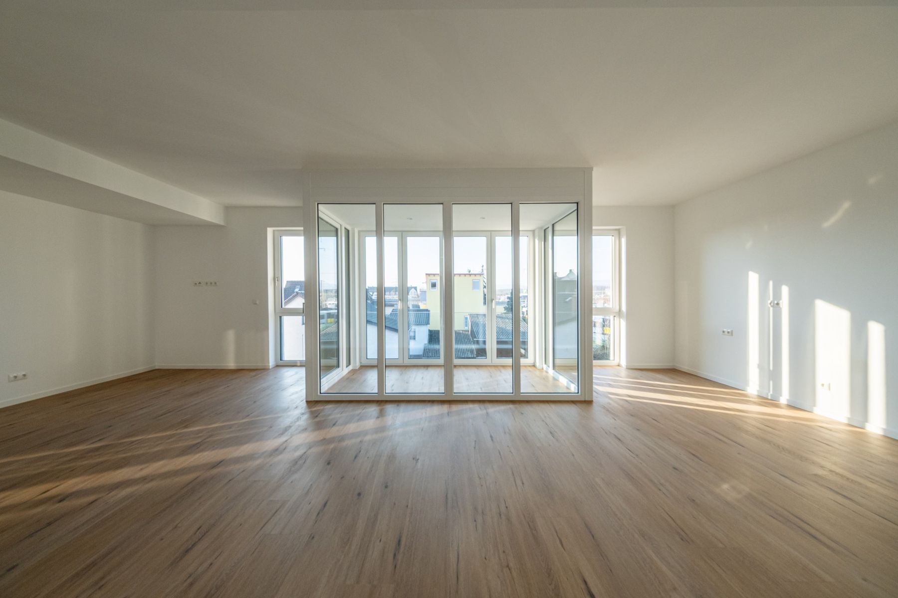 Mehrfamilienhaus K, leere Wohnung mit Parkettboden und raumhoher Fensterfront im Streiflicht