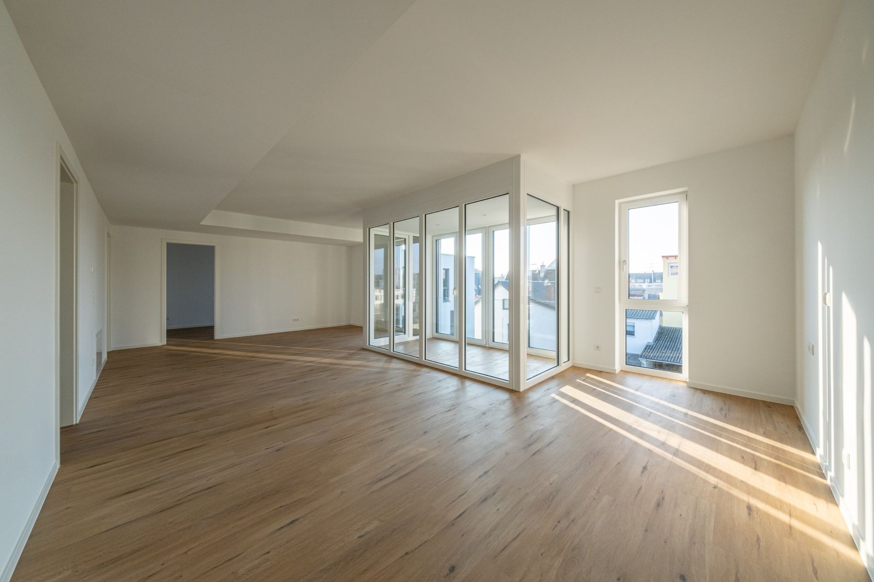 Mehrfamilienhaus K, großer Wohnraum mit Fensterfront und Sonnenstreifen auf dem Parkett